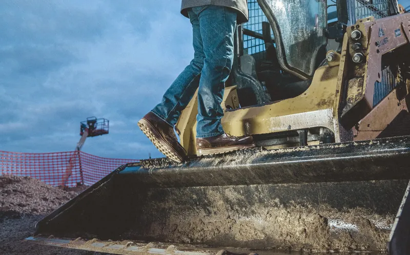 Crew member in Red Wing work boots stepping onto a skid steer on a Louisiana jobsite